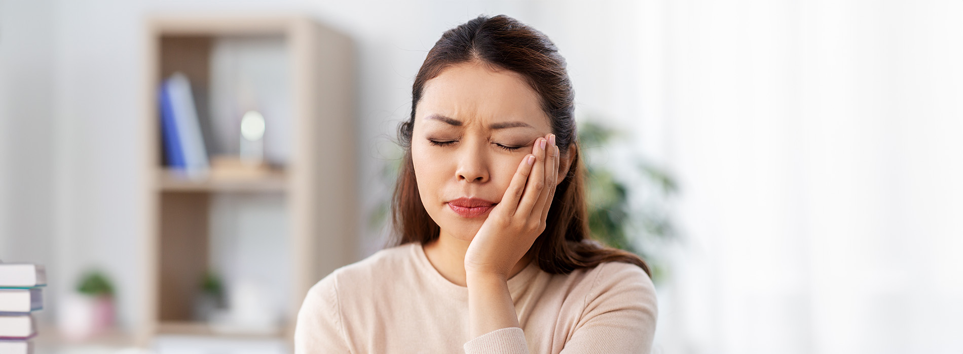The image shows a woman with her hand on her face, looking distressed, against a blurred background that suggests an indoor setting with books and a shelf.
