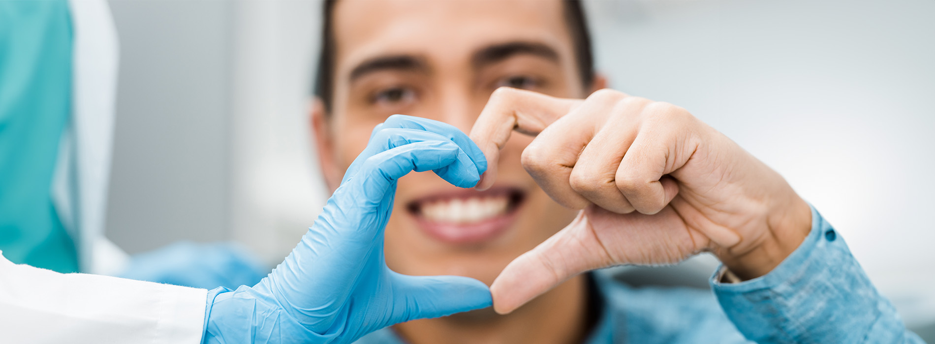 A person wearing gloves makes a heart shape with their hands while another person looks on, both are in a medical setting.