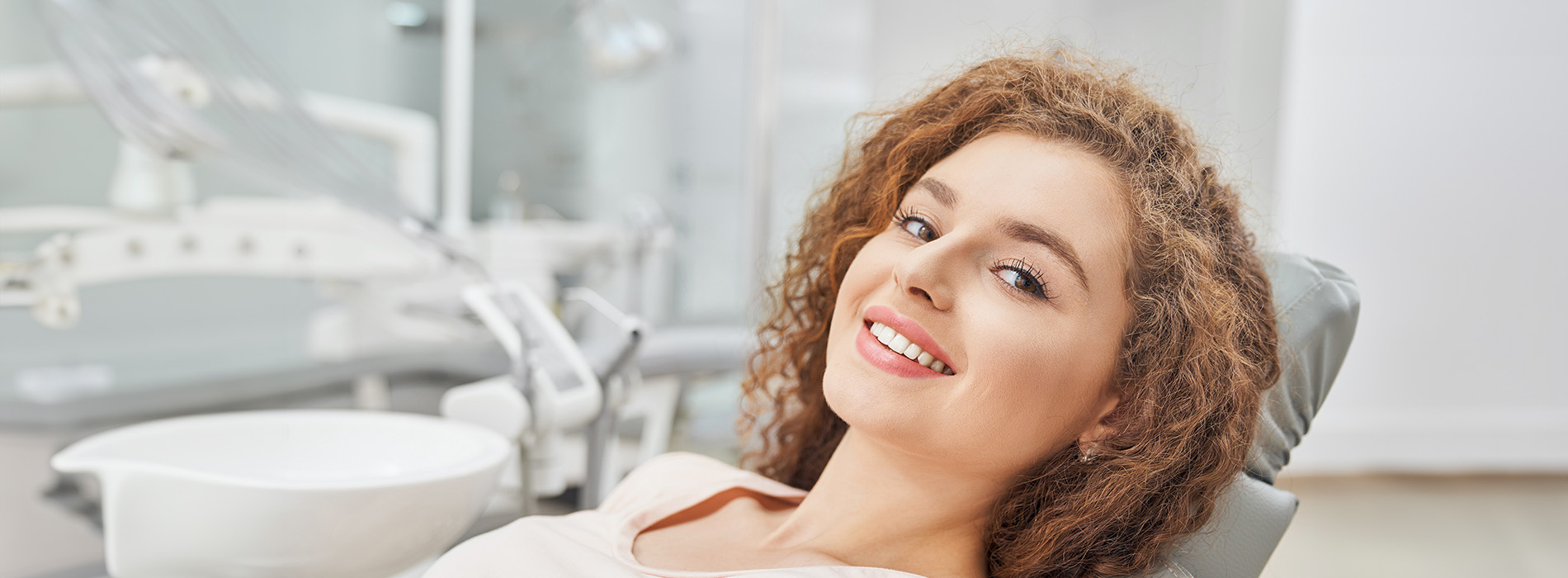 A smiling woman seated in a dental chair with dental equipment behind her.